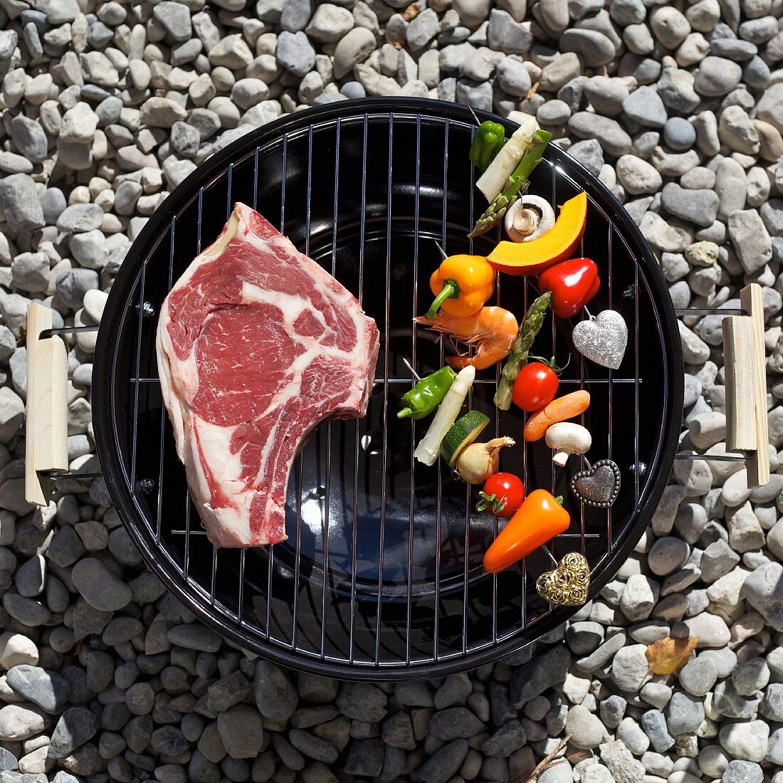 A raw T-bone steak and vegetables on a barbecue