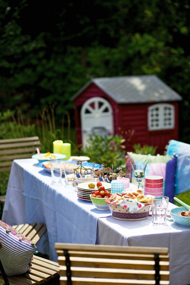 A table laid with cinnamon whirls and strawberries in the garden for a party on Midsummer day