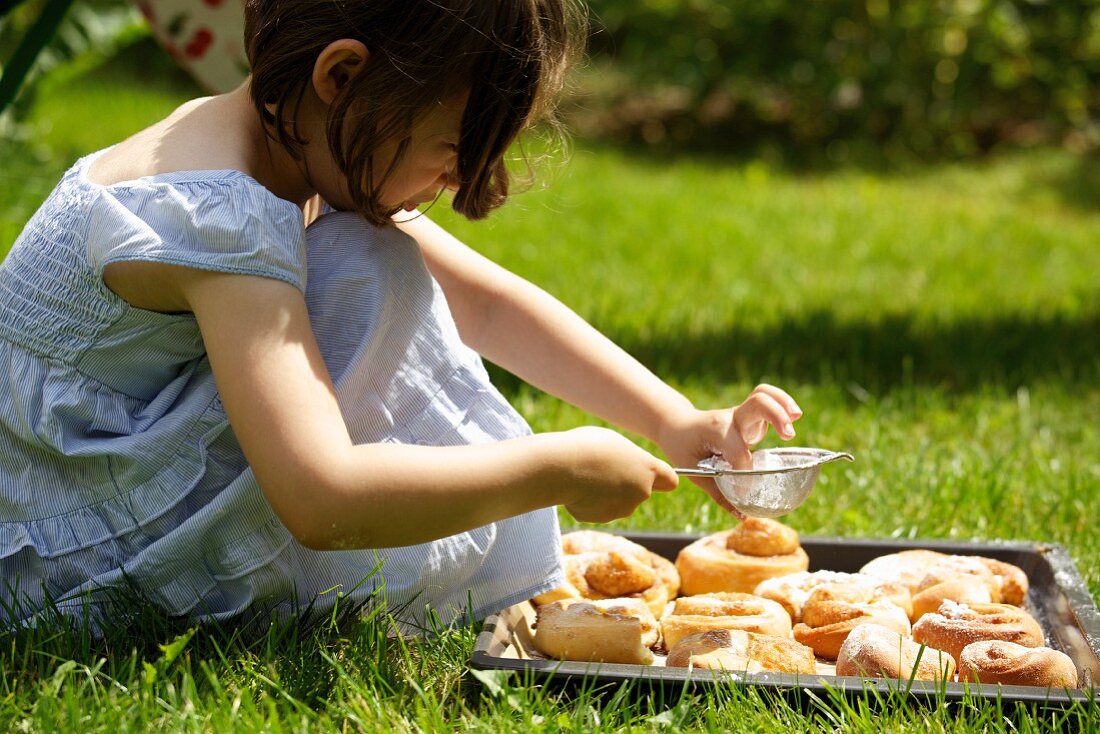 Mädchen bestäubt mit Puderzucker frisch gebackene Kanelbullar (Schwedische Zimtschnecken) auf dem Rasen