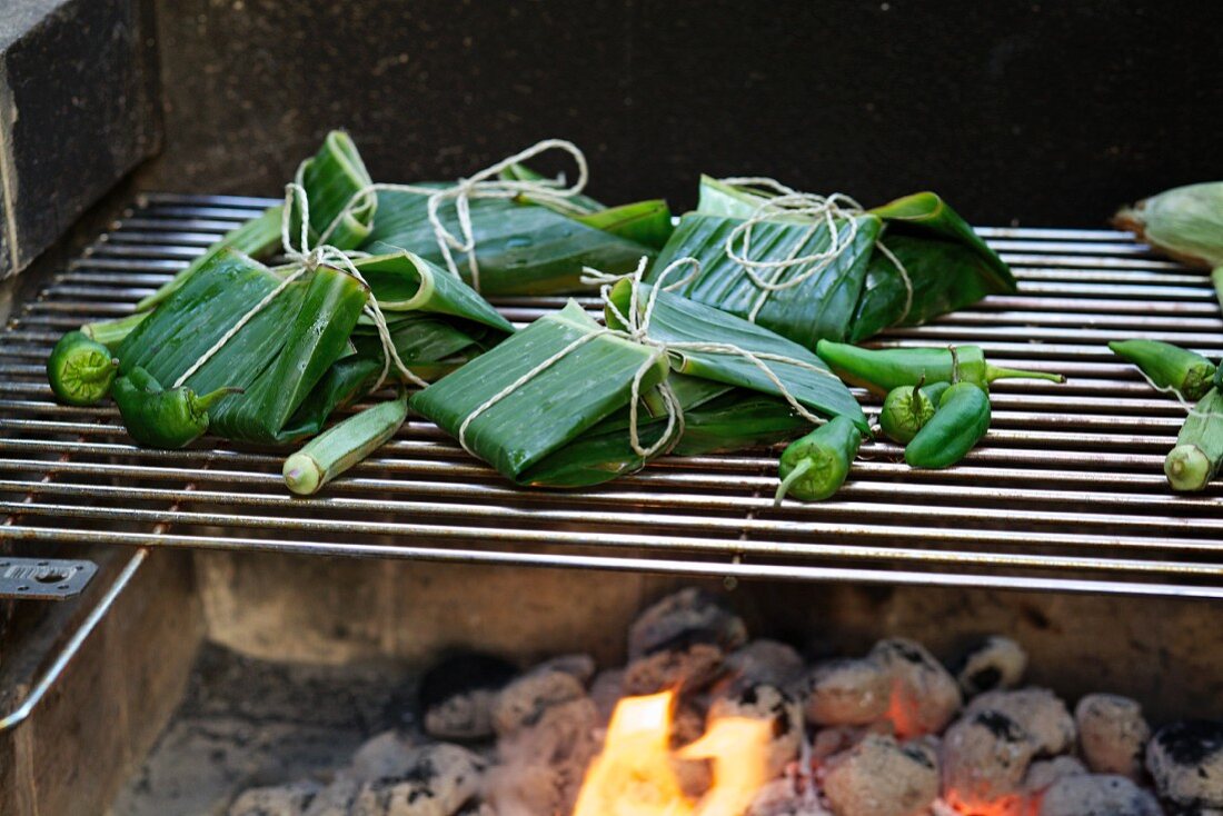 Fish parcels wrapped in banana leaves on the barbecue with vegetables