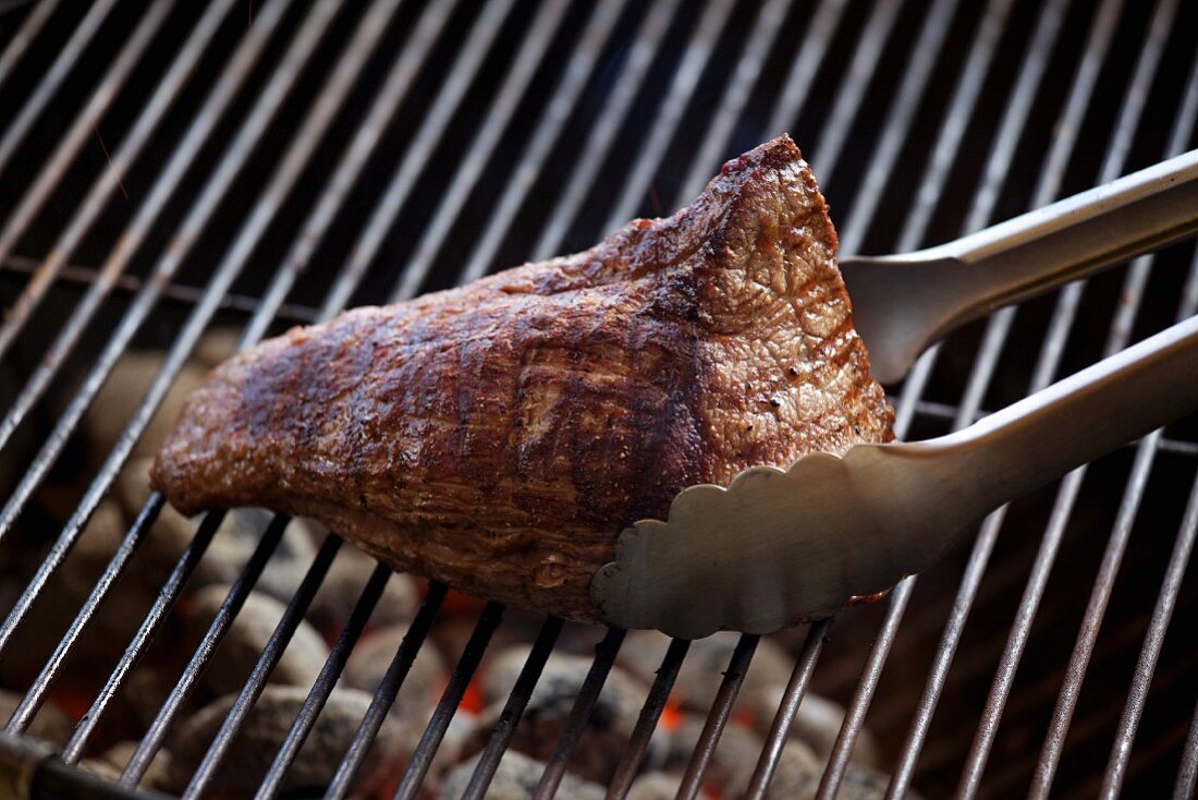 Steak mit Zange auf dem Grill