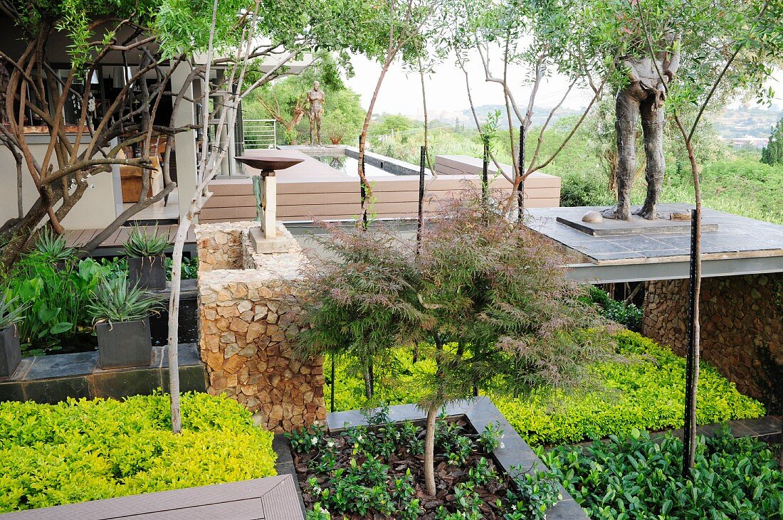 Garten mit Skulpturen, Pflanzbeeten und kleinen Bäumen in Hanglage