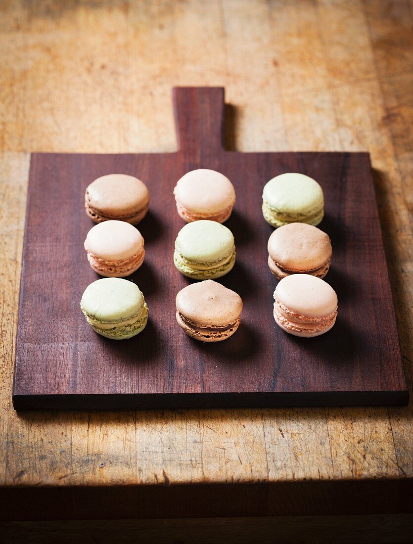 Verschiedene Macarons in drei Reihen auf einem Holzbrett