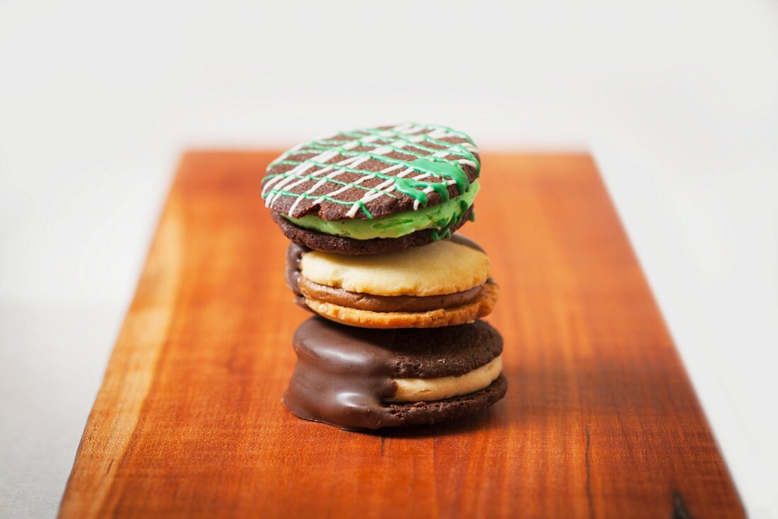 Three Assorted Sandwich Cookies Stacked on a Wooden Board