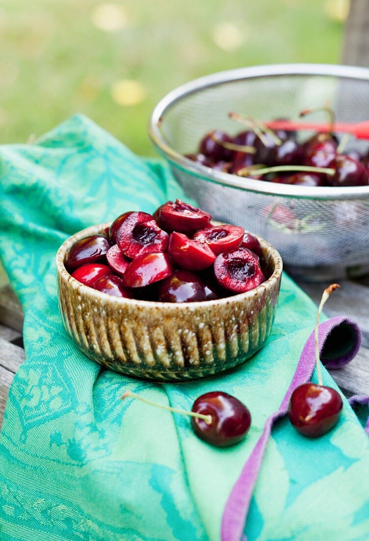 Fresh Cherries; A Bowl of Halved and Pitted Cherries and a Colander of Whole Fresh Ones