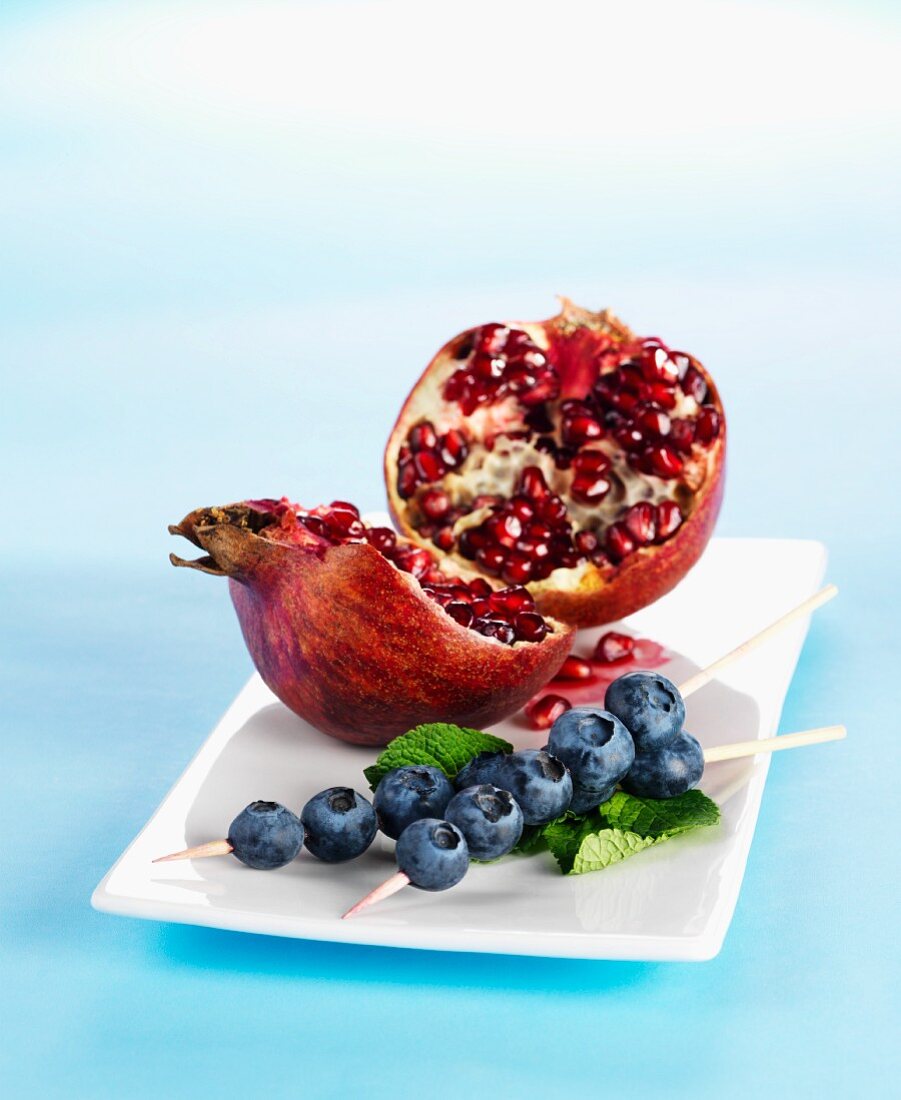 A broken-open pomegranate and skewers of blueberries