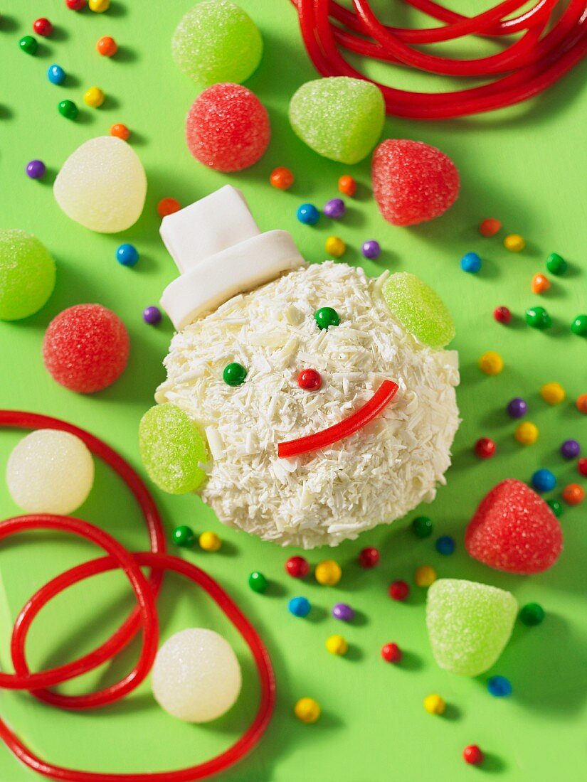 A coconut ball decorated to look like a snowman, with jelly sweets on a green surface