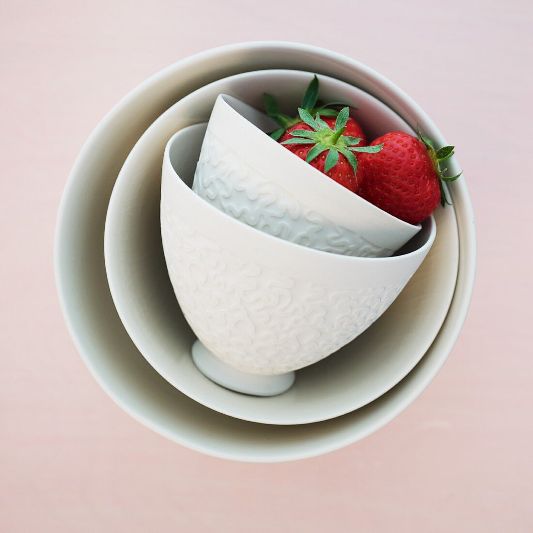 Two strawberries in white, overturned ceramic bowls