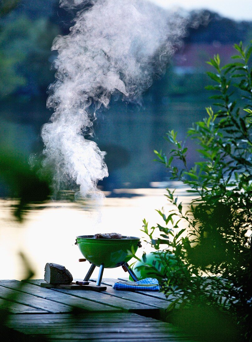 A smoking barbecue on a wooden jetty by a lake