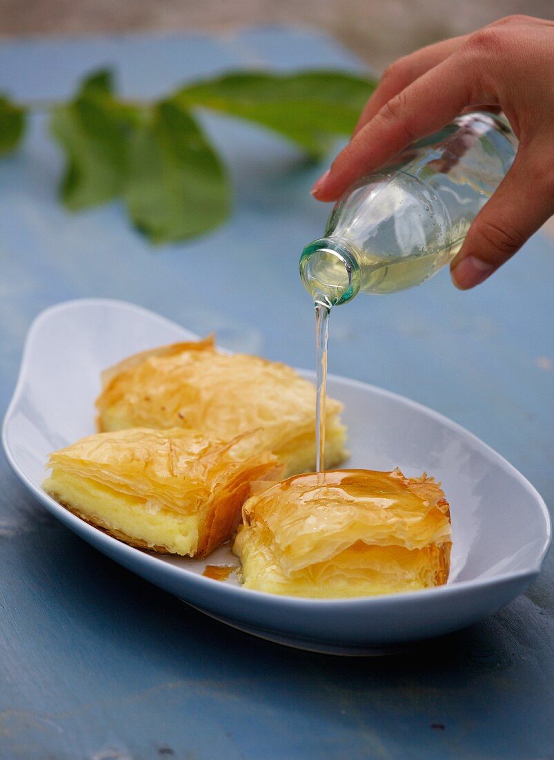 Galaktobouriko (semolina pudding in filo pastry, Greece) being drizzled with syrup