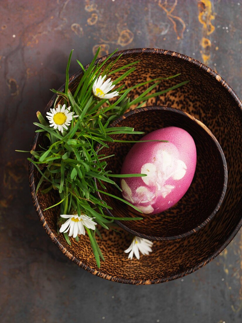 Pinkfarbenes Osterei in Holzschale mit Gänseblümchen