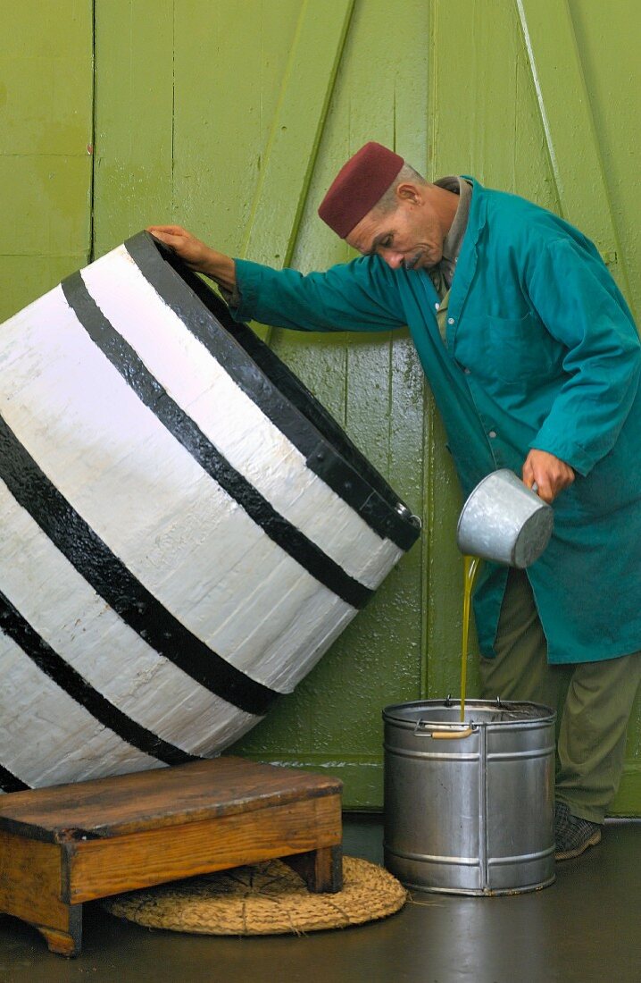 Mann schöpft Olivenöl aus Fass in einen Eimer (Tunesien)