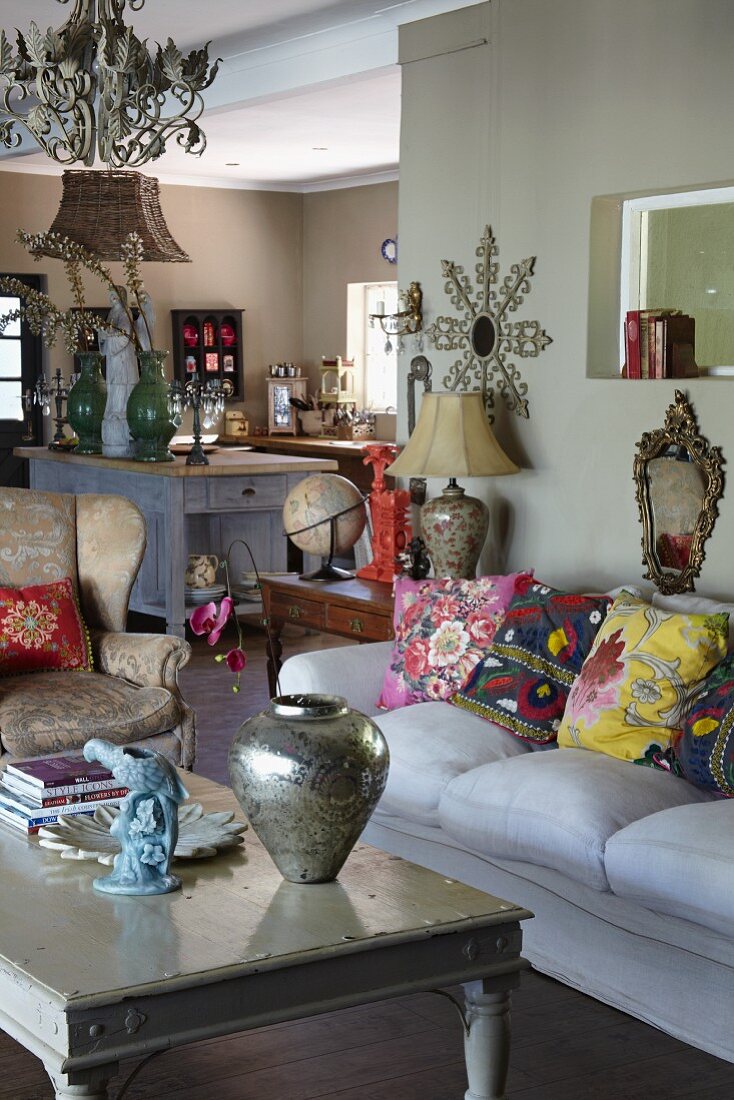 Silver vase on coffee table and ethnic scatter cushions on sofa in open-plan interior; kitchen area in background