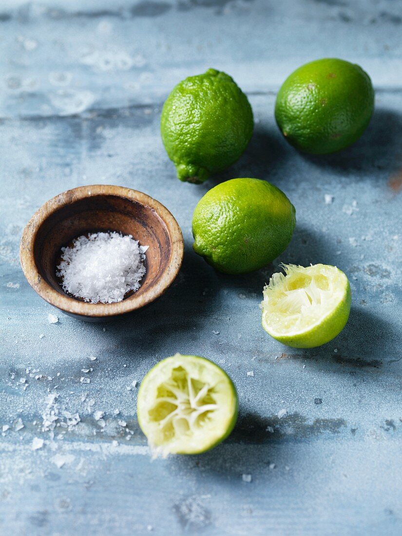 Whole limes and squeezed half limes with a small bowl of salt