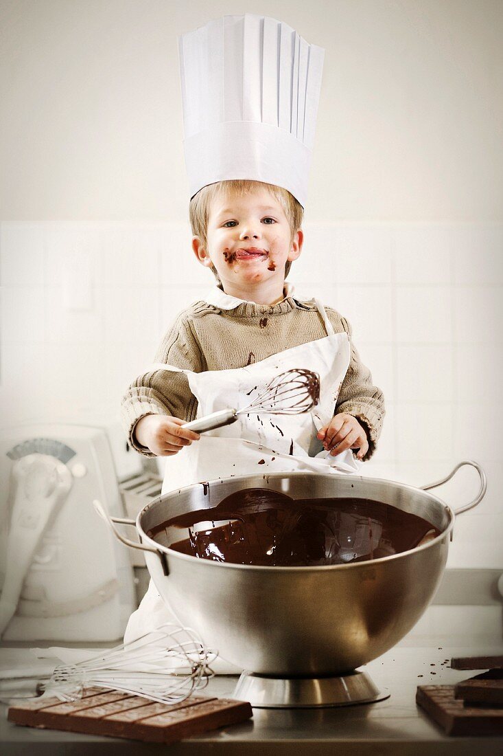 Junge mit Kochmütze vor Schüssel mit flüssiger Schokolade