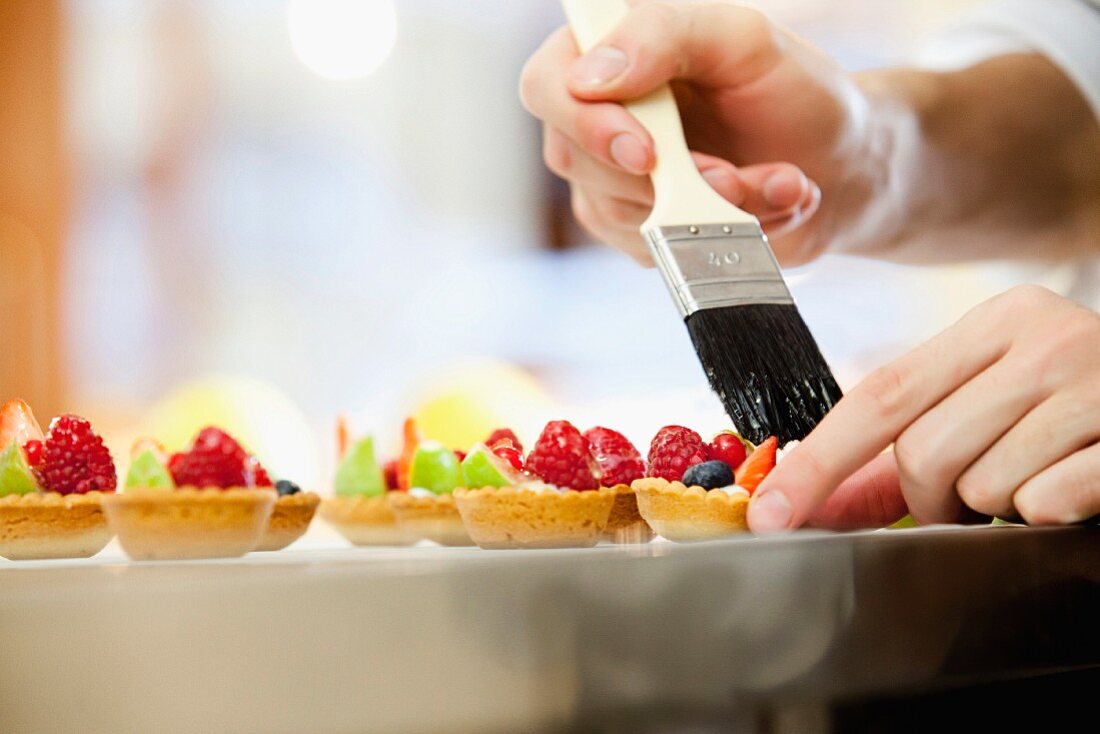 Small fruit tartlets being brushed with glaze