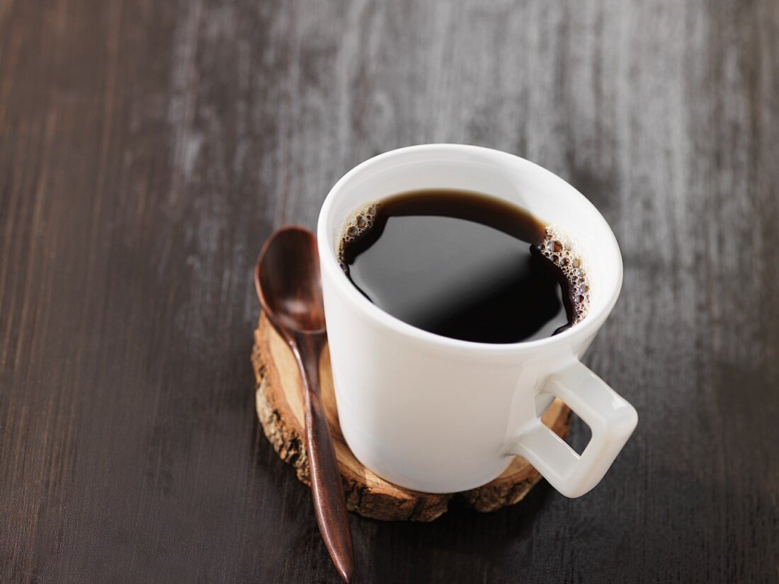 Black coffee in a mug on a disc of wood