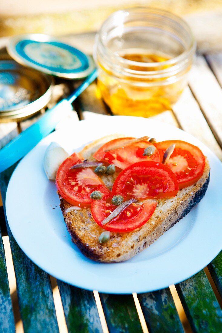 A slice of bread topped with tomatoes, capers and anchovies