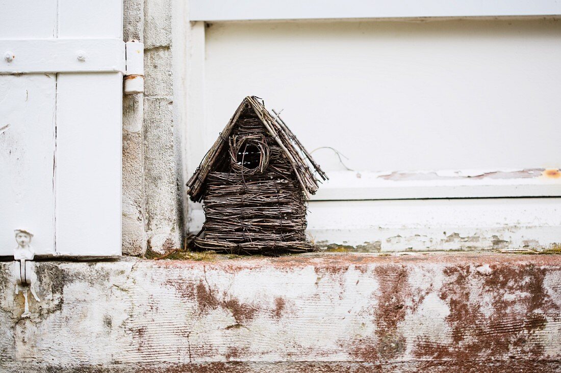 Vogelhäuschen aus Geflecht auf verwitterter Steinstufe am Haus