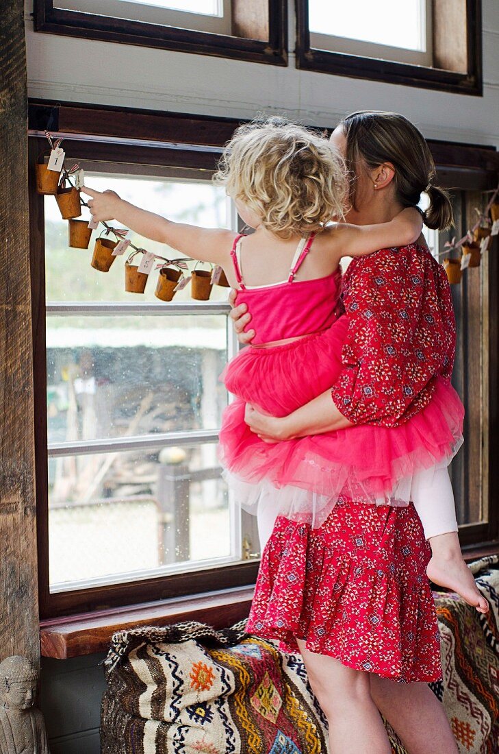 Mother and daughter looking at hand-crafted Advent calendar garland hanging in window
