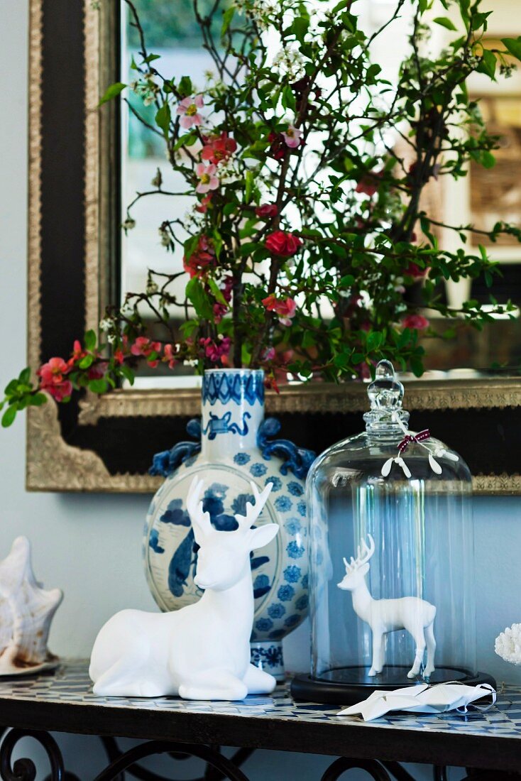White china stag figurines and ceramic vase of flowering branches in front of elegant mirror