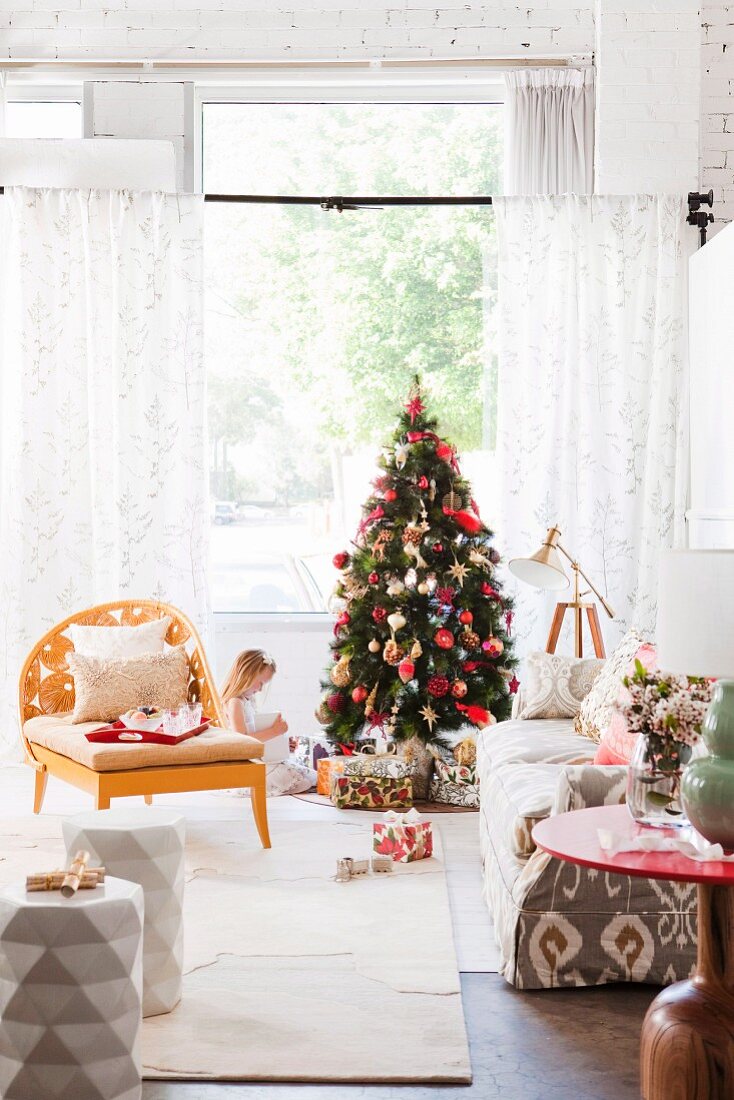 Armchair and sofa in living room; little girl sitting next to Christmas tree and piles of presents in background