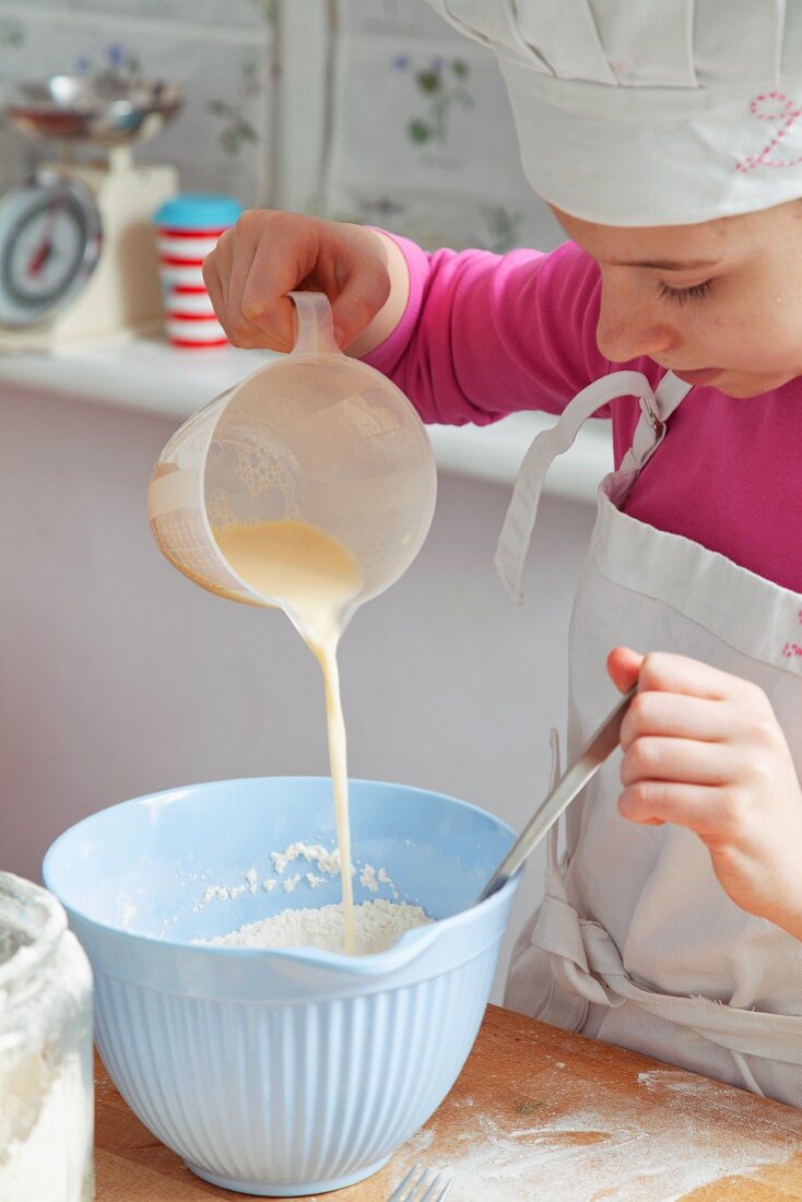 A girl pouring milk into a bowl of flour
