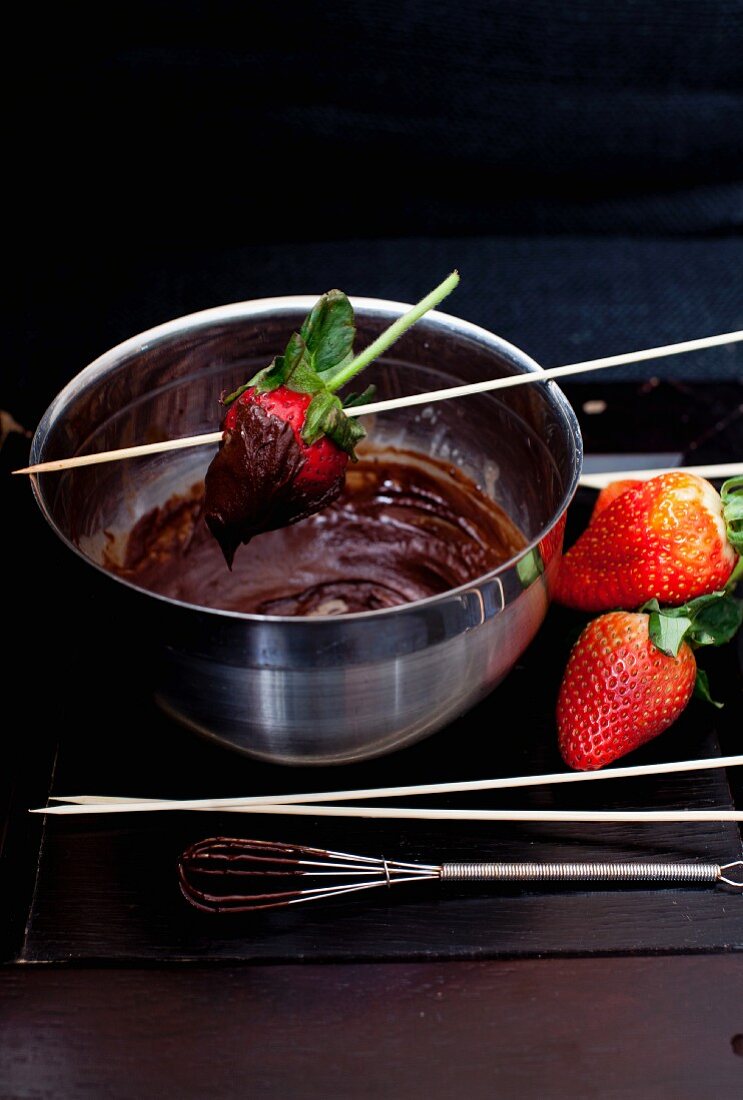 A Bowl of Melted Chocolate with Strawberries for Dipping; A Chocolate Covered Strawberry in the Bowl
