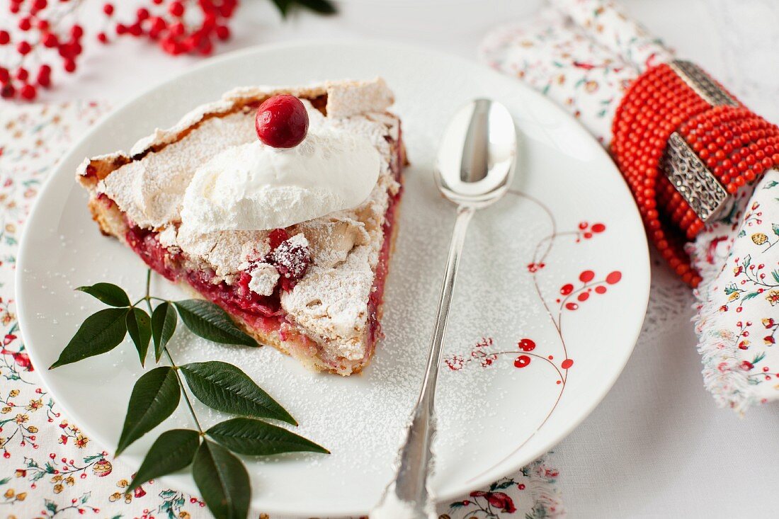 Ein Stück Cranberry-Baiser-Tarte auf Teller mit Puderzucker