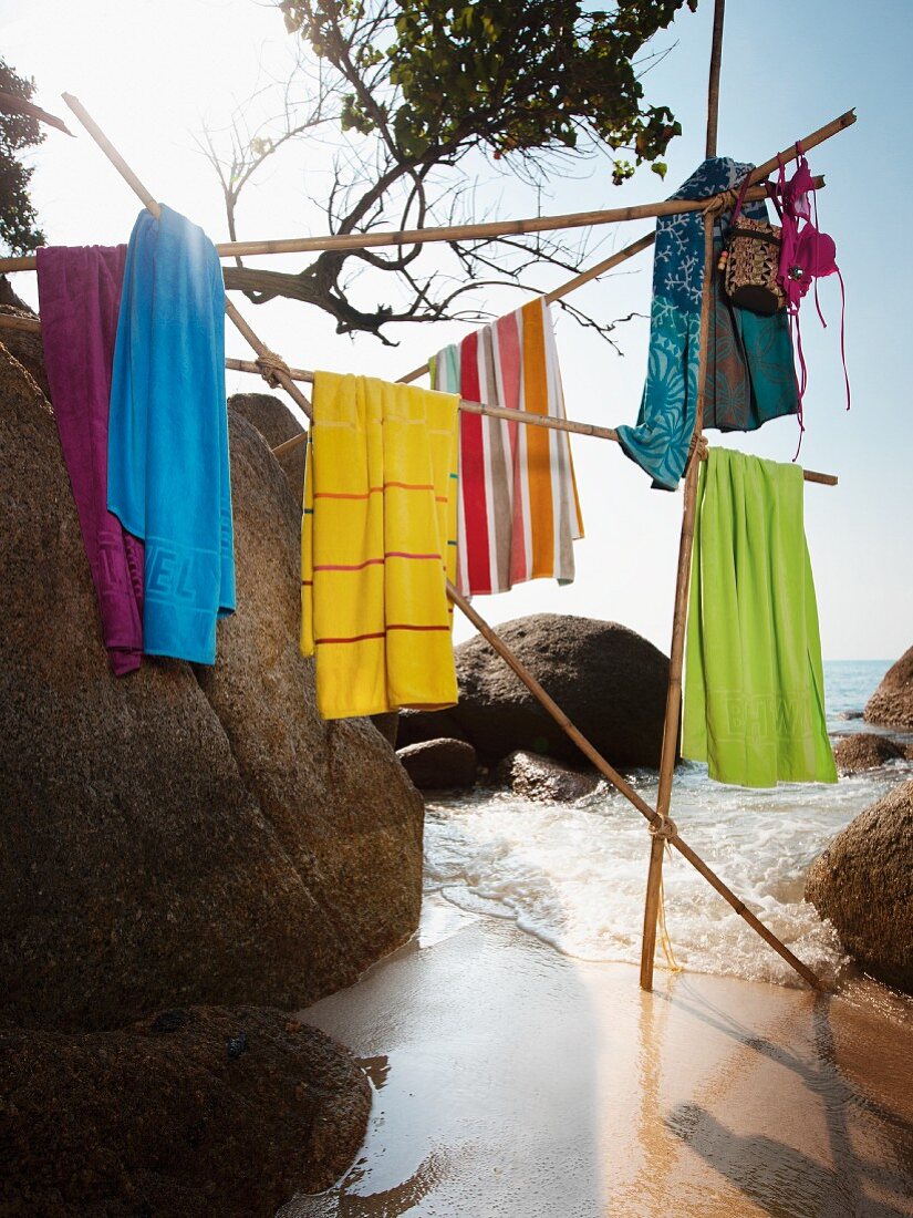 Badetücher hängen auf Stangenkonstruktion zwischen Felsblöcken am Meeresstrand
