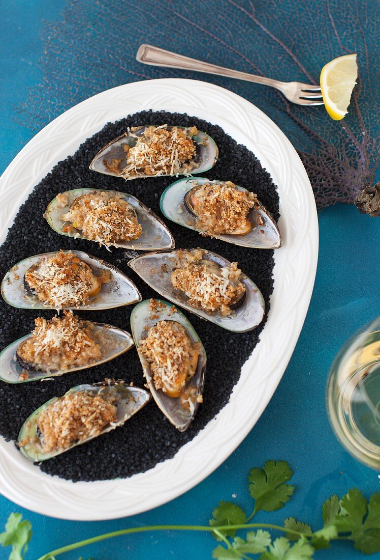 Green mussels topped with cheese and grilled, on a white plate with black salt