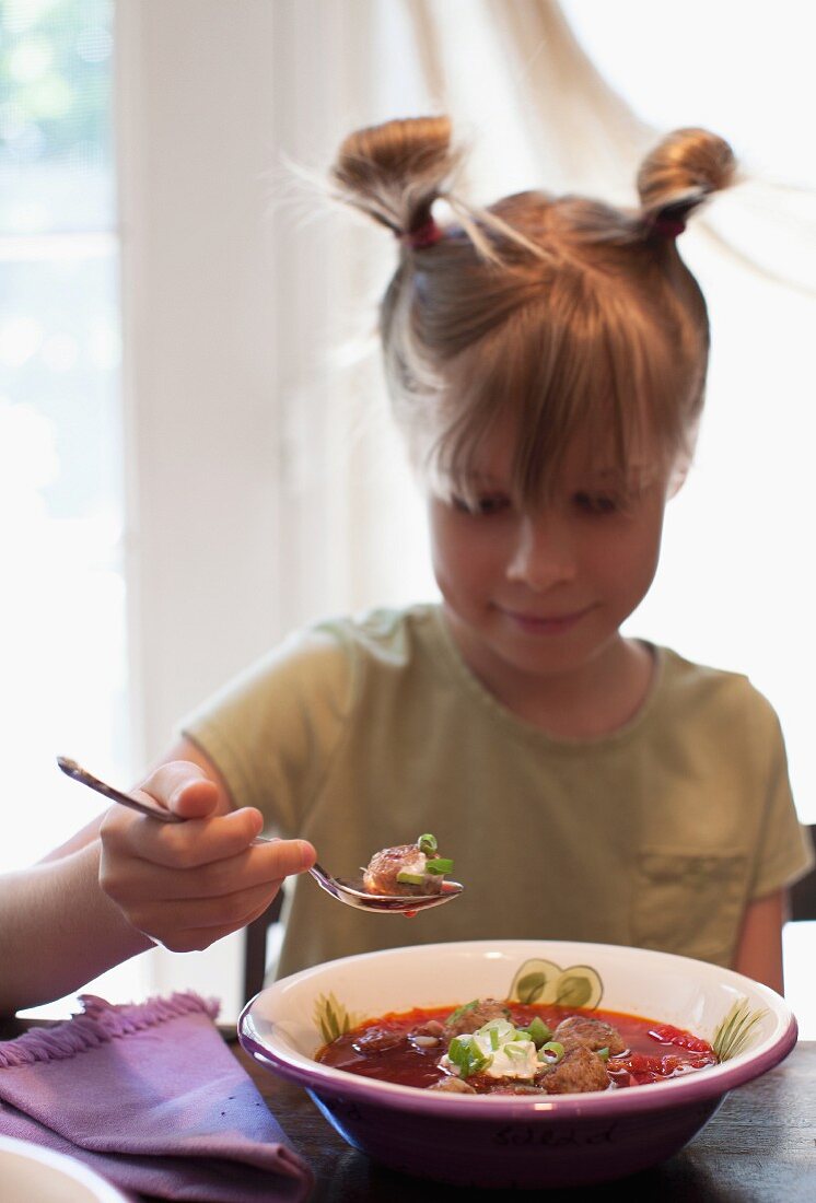 Girl Eating a Bowl of Soup with Meatballs