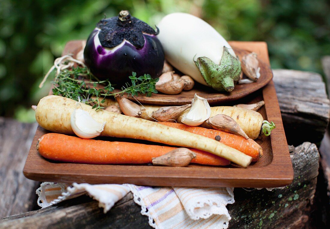 Fresh root vegetables, garlic and aubergines for soup on a wooden tray