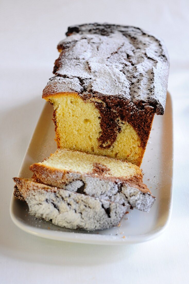 Marble cake with icing sugar, partly sliced