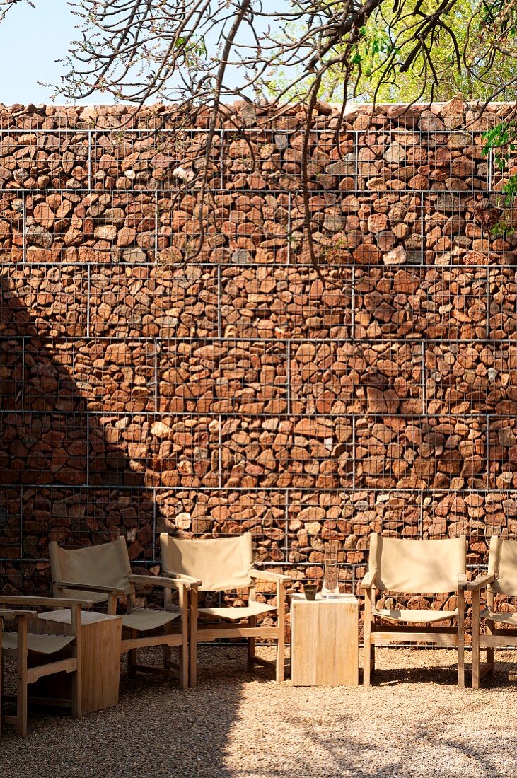 Gabion wall behind wire mesh; in front a circle of comfy armchairs with a side table
