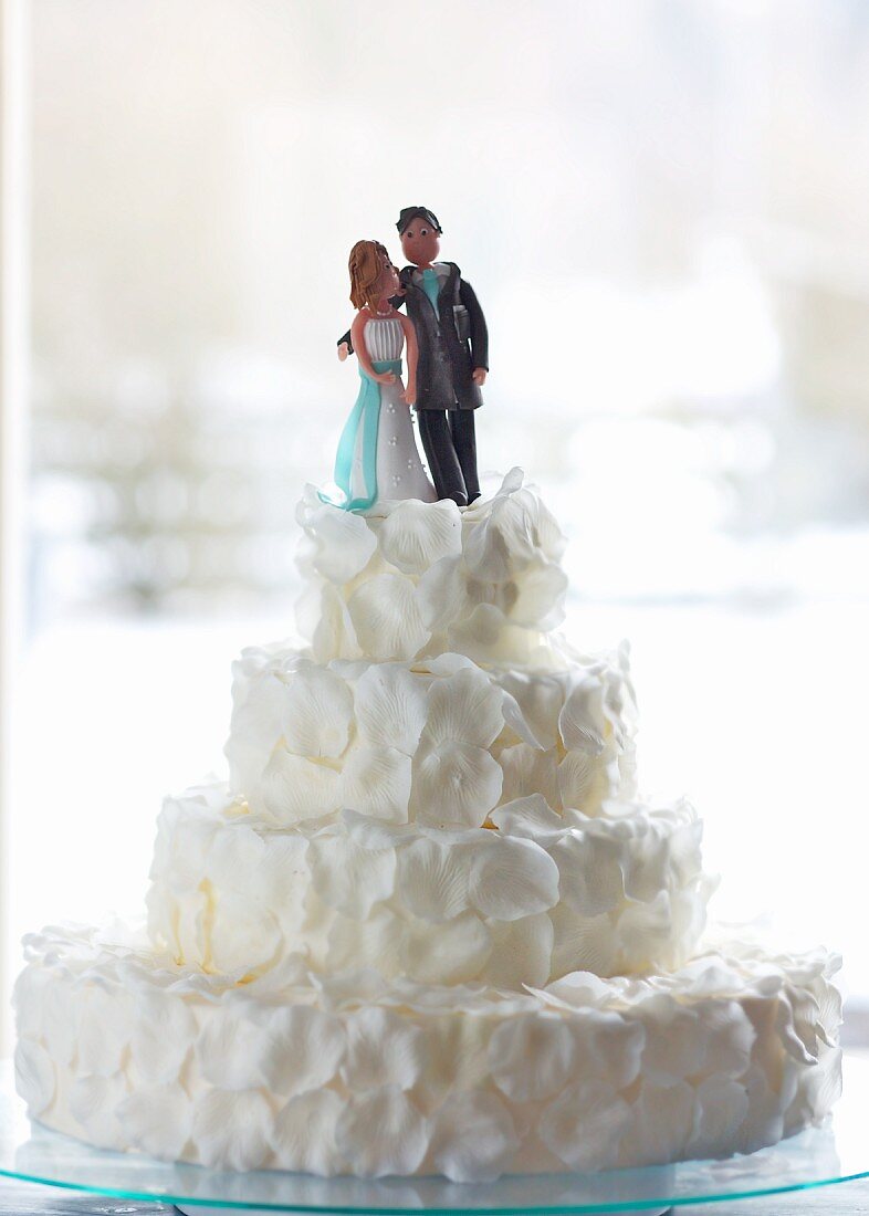 An original wedding cake decorated with white rose petals and a bridal couple in marzipan
