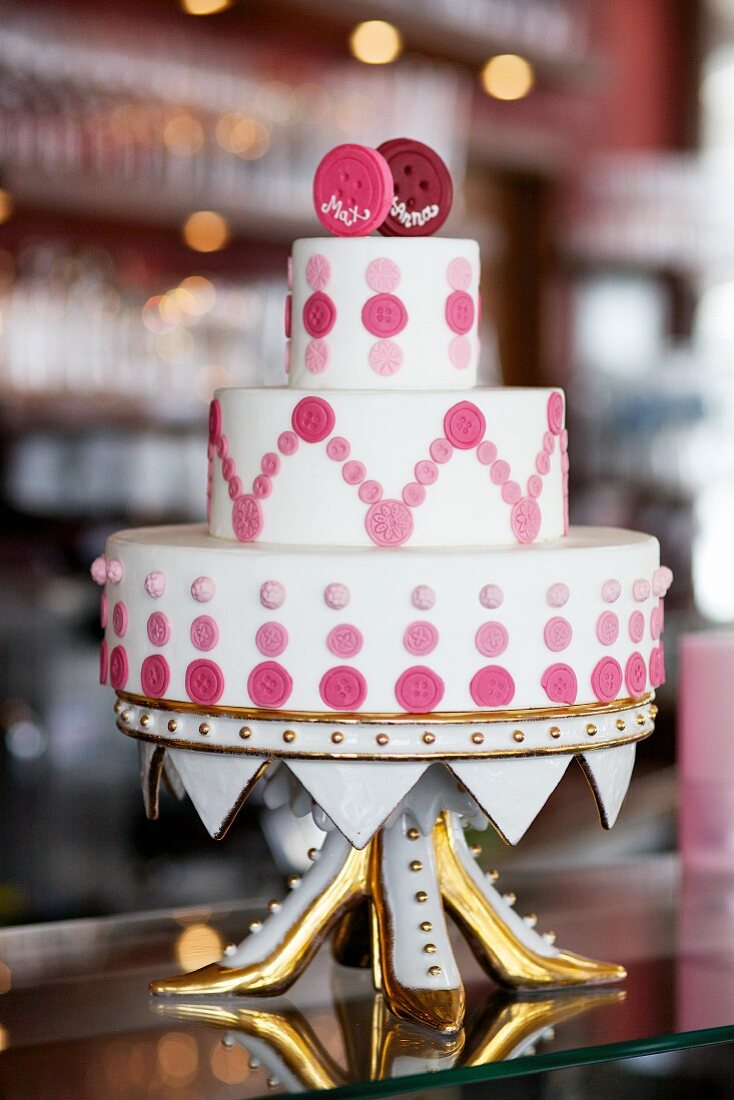 Unkonventionelle Hochzeitstorte mit pinkfarbener Knopfdekoration auf vergoldeter Etagere