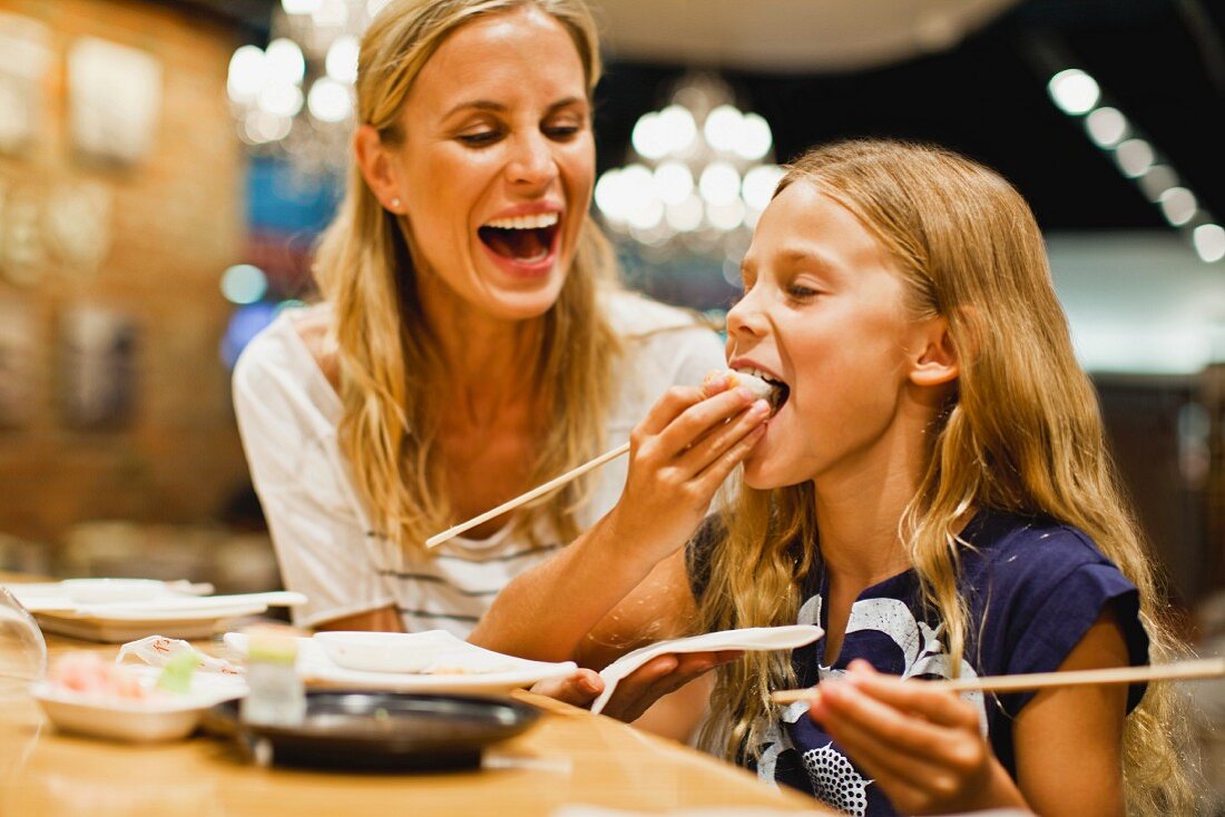 A mother and daughter eating sushi with chopsticks
