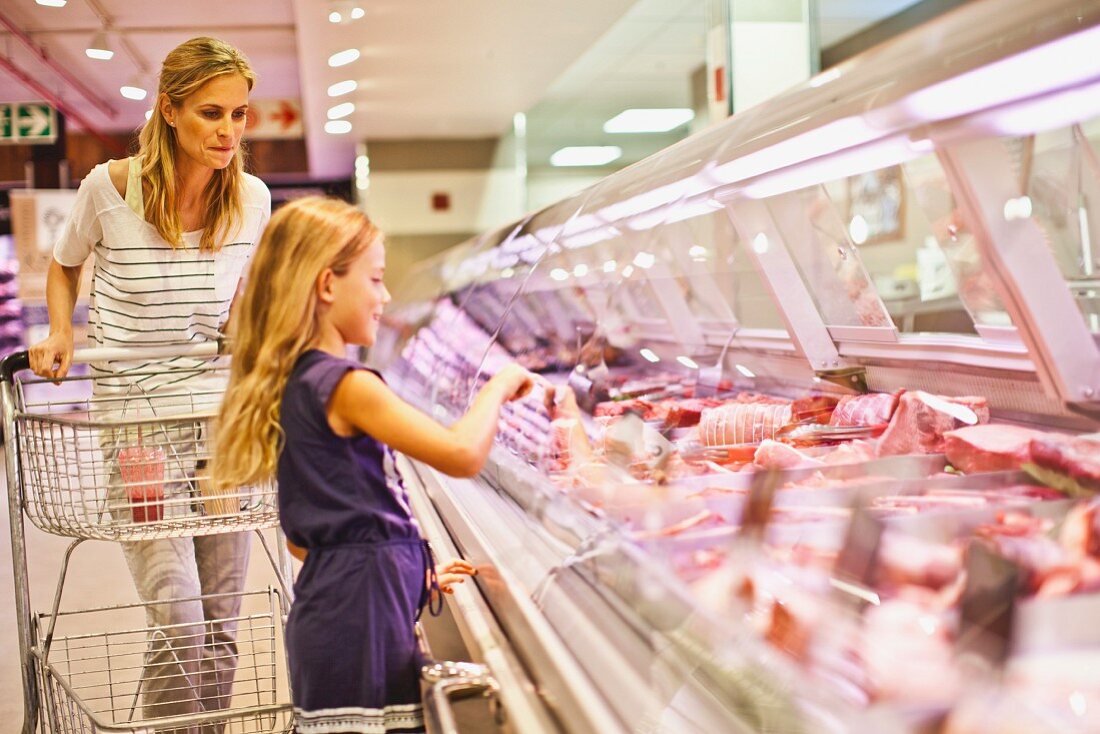 Mutter und Tochter bei der Fleischvitrine im Supermarkt