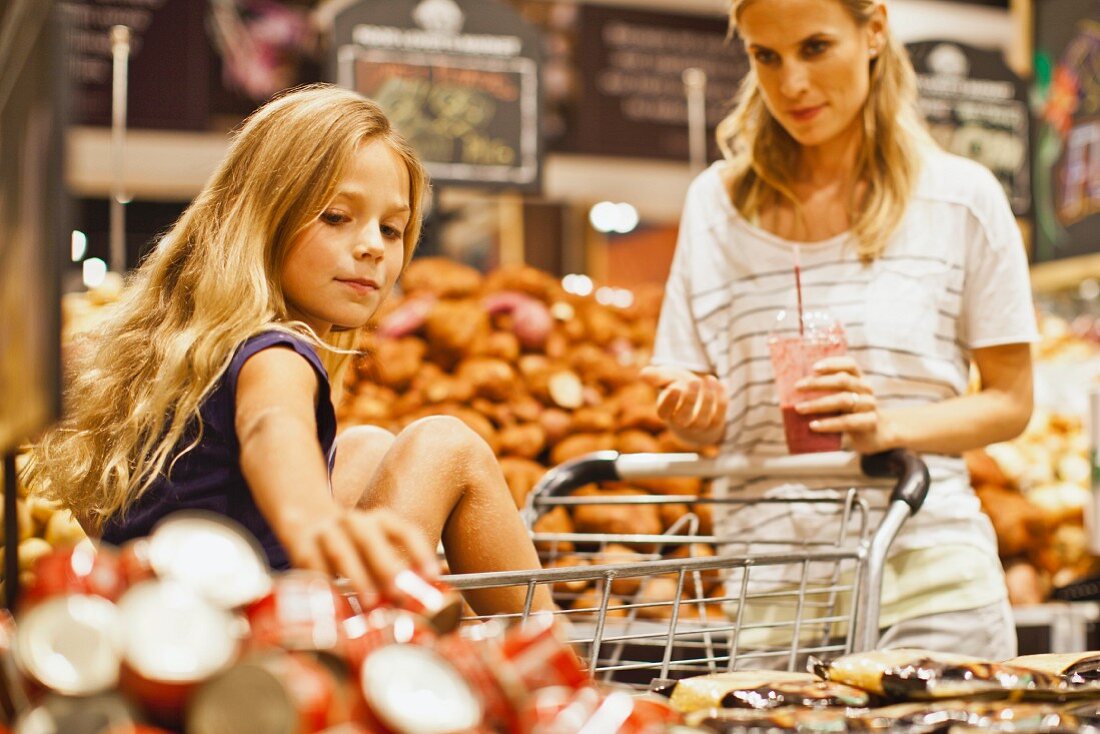 Woman and a young girl with a shopping trolley walking down a supermarket aisle