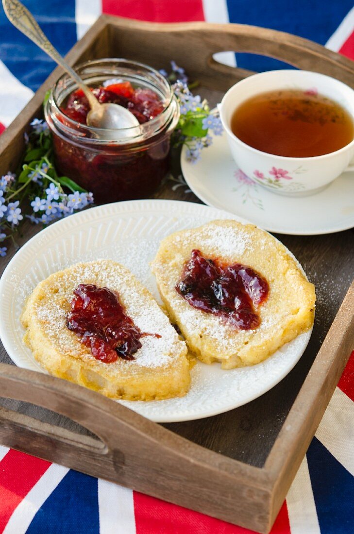 French toast with jam and a cup of tea on a wooden tray on top of a Union Jack flag