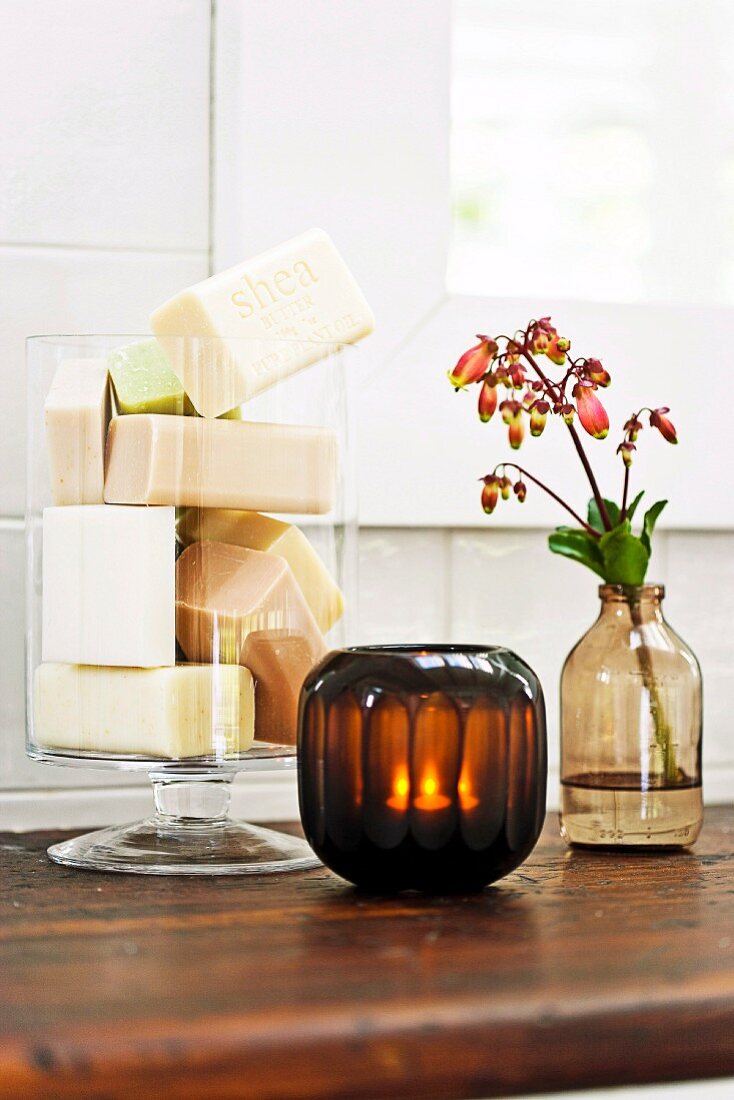 Blocks of soap in glass vessel, tealight in dark lantern and flowering branch in vase