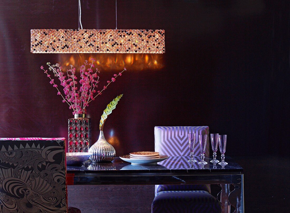 Crystal chandelier above Champagne glasses, shiny silver vase and vase of pink flowers on elegant dining table