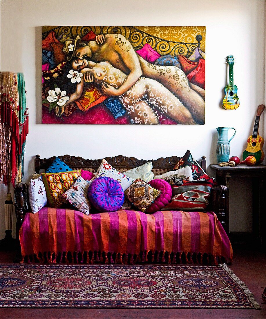 Antikes Sofa mit farbenfroher Decke und Kissensammlung unter buntem Gemälde mit Liebespaar