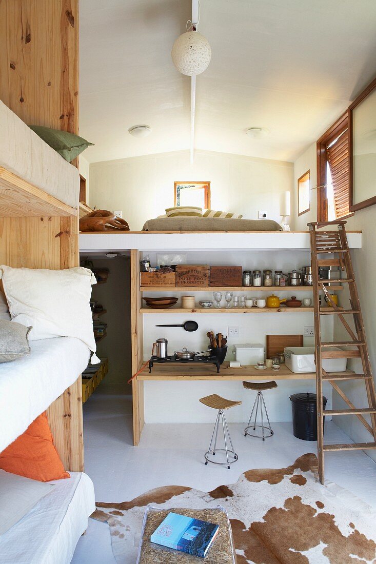 Multifunctional interior with cowhide rug on floor in front of improvised kitchen fittings below sleeping gallery