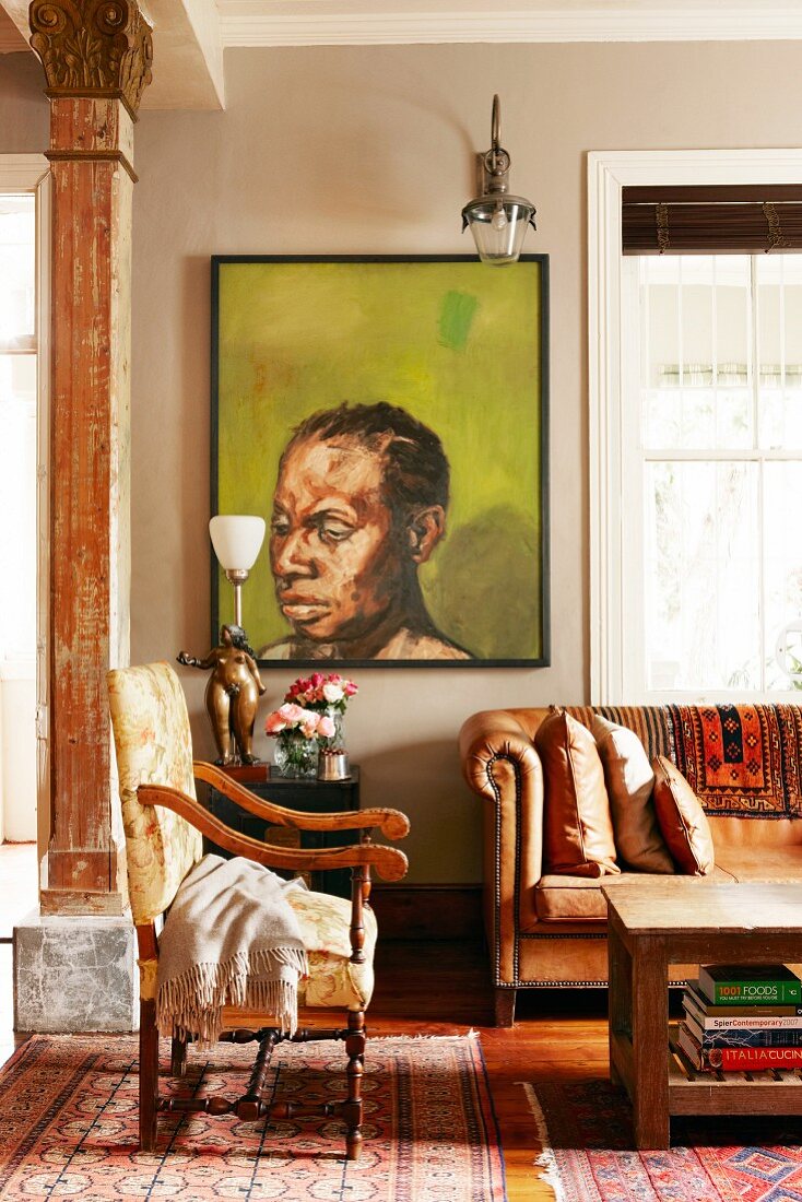 African painting behind vintage seating area with leather sofa and antique armchair on traditional Oriental rugs
