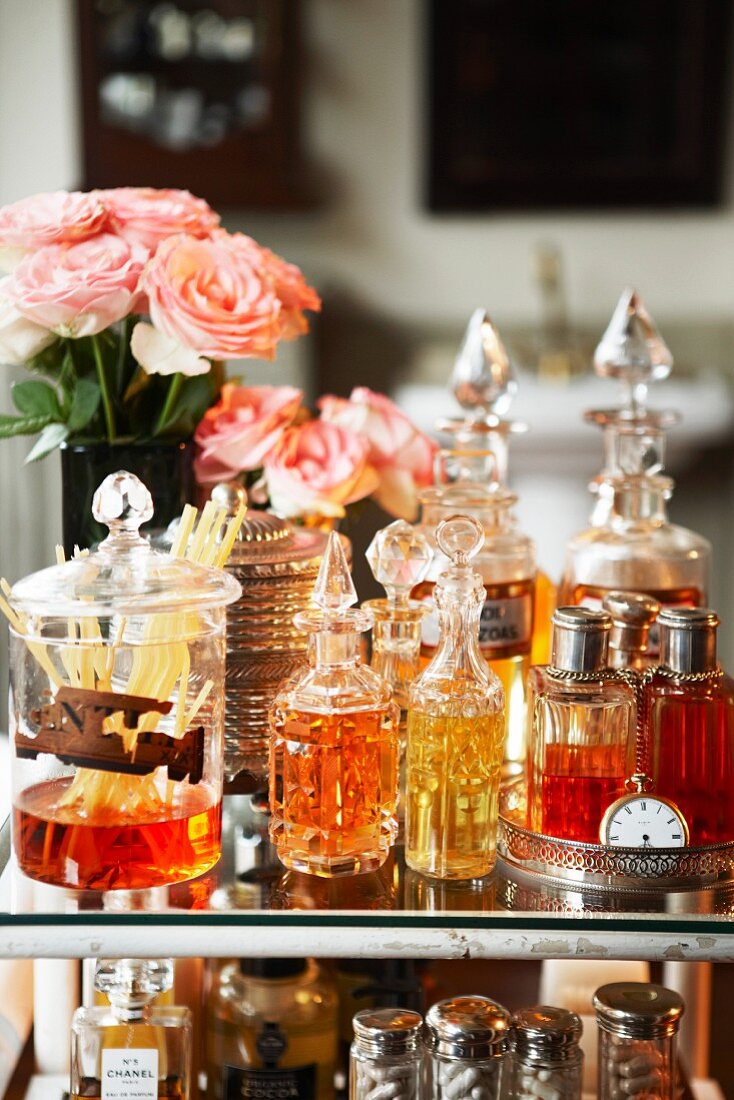 Perfume bottles, room fragrance diffuser and vases of roses on glass table top