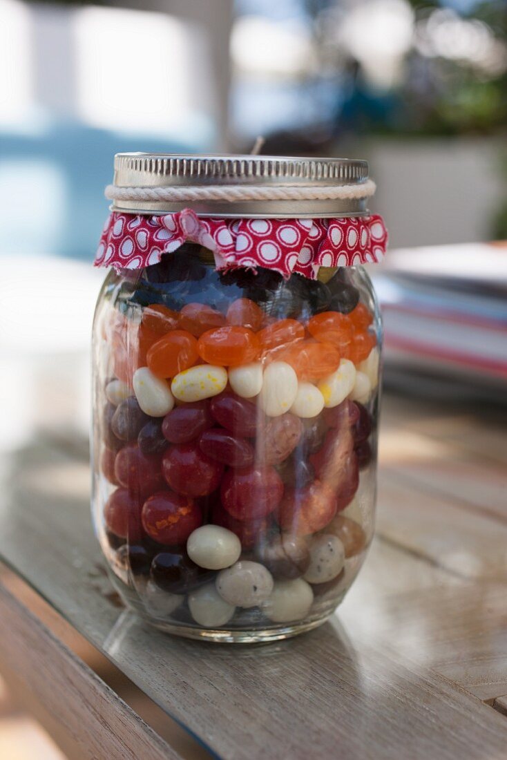 Verschiedene Süssigkeiten (Jelly Beans, Lakritze- und Schokodragees) in einem Einmachglas als Geschenk