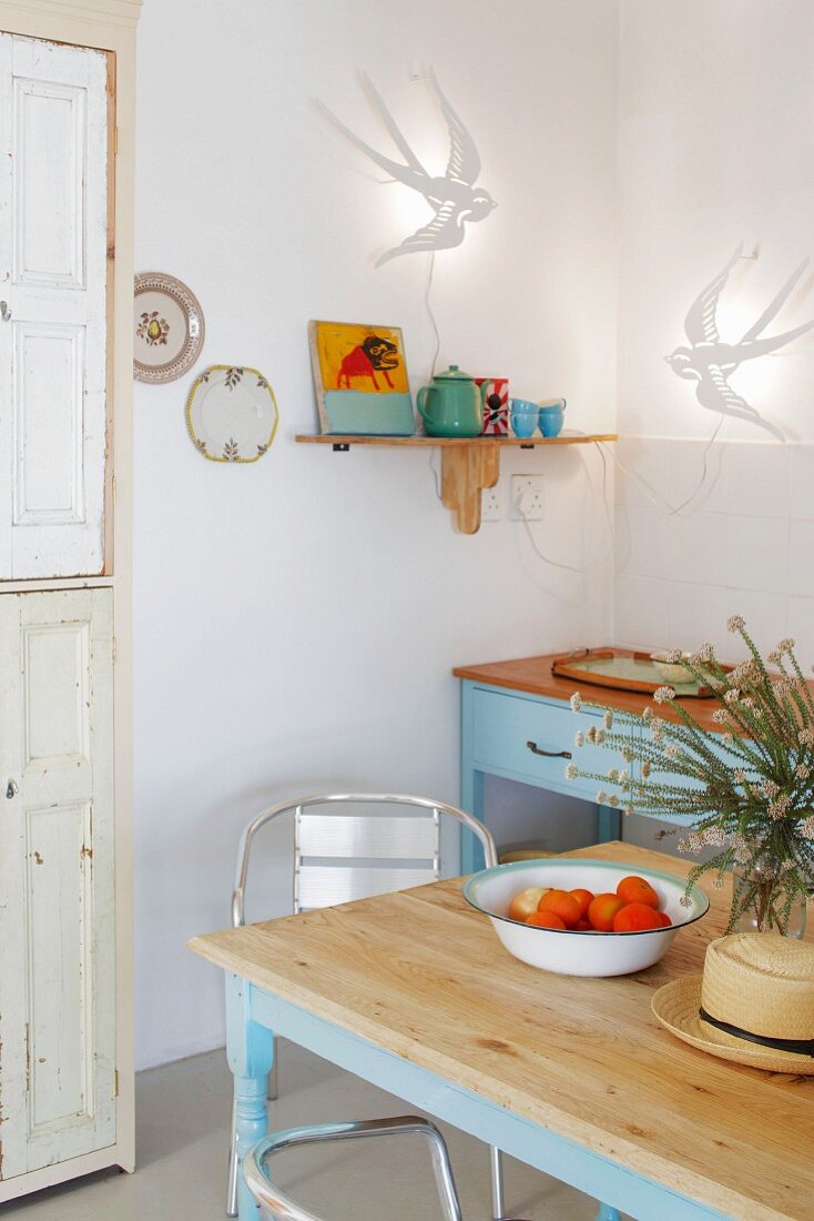 Kitchen table with pale blue frame in front of vintage kitchen counter in corner below swallow-shaped sconce lamps