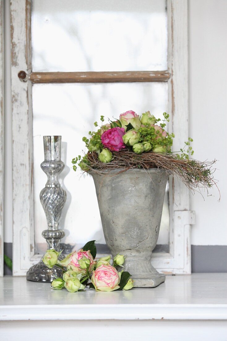 Rosendekoration mit Vasen aus Stein und Glas vor altem Fensterflügel